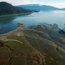 Aerial view of coastal wetland at low tide with snow capped mountains in the background.