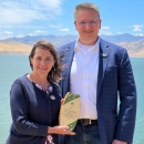 two people stand outside for a photo with a wooden award