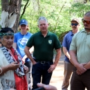 A woman in traditional Native American clothing speaks with several people wearing federal- or state-agency shirts and hats