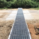 Metal grate running across a road with adjacent ground covered in straw.