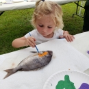 A little girl chooses orange from her palette of colors and is painting a real fish. She will use the painted fish to create her Fish Art T-shirt. 