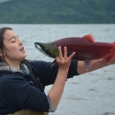 Aquatic Science Academy student holds a red salmon in front of her face. 