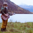 A woman playing guitar next to a lake