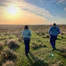 two people walking towards sunset through sagebrush landscape