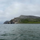 Crowbill Point, covered in green and grey with grass and dirt, stretches into the blue waves of the Chukchi Sea.