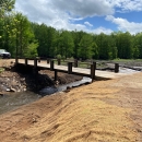 A bridge over a free-flowing creek with burlap covered soil for replanting on the banks