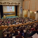 auditorium filled with people with large screen above the stage