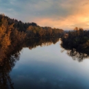A glowing sky is reflected in Lake River that has fall vegetation along it