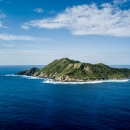 A mountainous island covered in green vegetation emerges from bright blue water