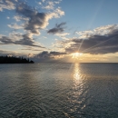 Sun breaking through clouds over a lake.