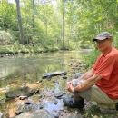 A man sitting alongside a creek.