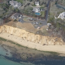 an aerial view of an eroding coastal bluff on a national wildlife refuge property. Buildings, a parking lot and trees can be seen surrounding the property