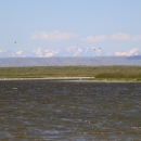 A lake is shown in the foreground with mountains in the background of this photo as ducks fly in the distance.