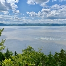 A blue sky with clouds as the sun shines on the upper Mississippi River with green bluffs in the distance.