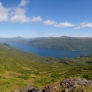 Cerulean blue water stretches between sloped mountains beneath a partly cloudy sky.