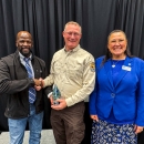 A unformed FWS employee shakes hands with another individual while holding an award. A woman stands smiling to the right of the awardee.