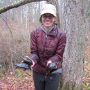 A woman stands in the woods holding two turtles in each hand