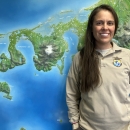 Woman with long hair in a FWS uniform standing in front of a wall map