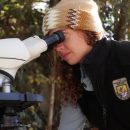 Madison wearing a tan toboggan and a black jacket with USFWS emblem looking through binoculars