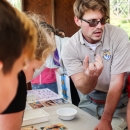 Male biologist holding hand up while talking to students