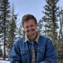 a man with a mustache stands in a pine forest