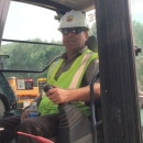 Phil Herzig with USFWS hard hat and work vest inside cab of excavator.