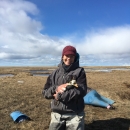 Woman in outdoor clothing on tundra holding a spectacled eider