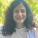 A woman with dark curly shoulder length hair smiling