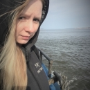 A close-up of a woman standing on a boat with water and sky behind her