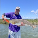 Jeff smiling holding a large fish in white shorts and a blue jacket