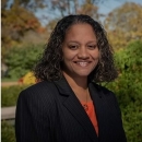 Lorisa smiles in a black blazer and orange blouse 