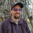 man in brown jacket stands near a tree