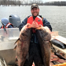 Man on boat smiles and holds up 2 carp