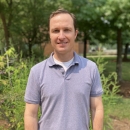 a man stands outside with trees in the background