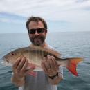 A man smiling holding a fish with orange and red fins