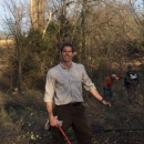 Headshot photo of Scott Hamilton in his uniform with a saw in hand standing next to a fallen tree by USFWS.