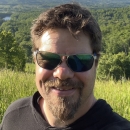 a selfie of a man wearing sunglasses with a green landscape behind him