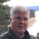 man with white hair stands near a snowy lake