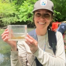 Jenna holding a viewing box with coal darters in it. Creek is in the background.