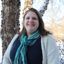 a woman wearing a scarf and sweater smiles and stands outside