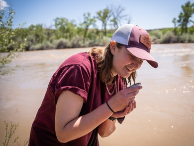 A person smiling while holding a razorback sucker. River in background.