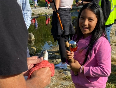 Little girl smiling with a fishing pole in front of a stream