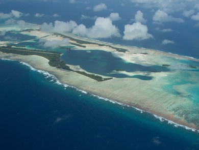 Aerial view of an island atoll surrounded by sandy reef in the deep blue ocean