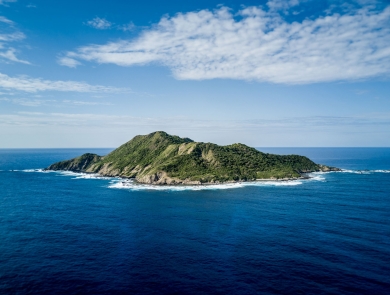 A mountainous island covered in green vegetation emerges from bright blue water