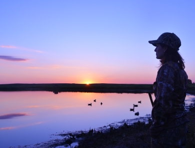 person waterfowl hunting by a wetland at sunrise