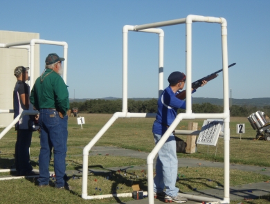 Boy aims sporting rifle at targets while standing behind a mobile range stand. 