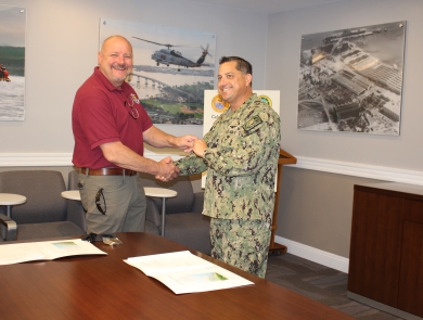 two men shake hands while standing behind large table