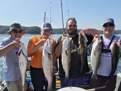 4 men holding striped bass on a boat