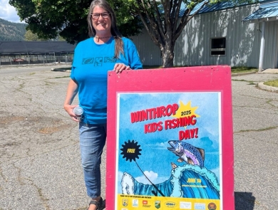 A woman in a blue shirt stands next to a red sign reading "Winthrop Kids Fishing Day"