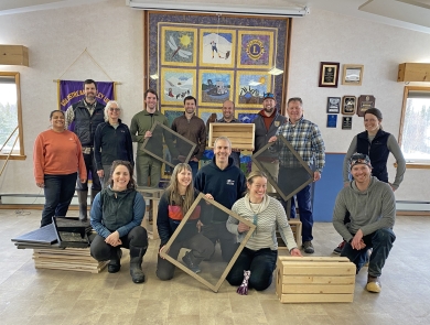 Fourteen people pose for a photo holding wooden boxes and frames with screens.